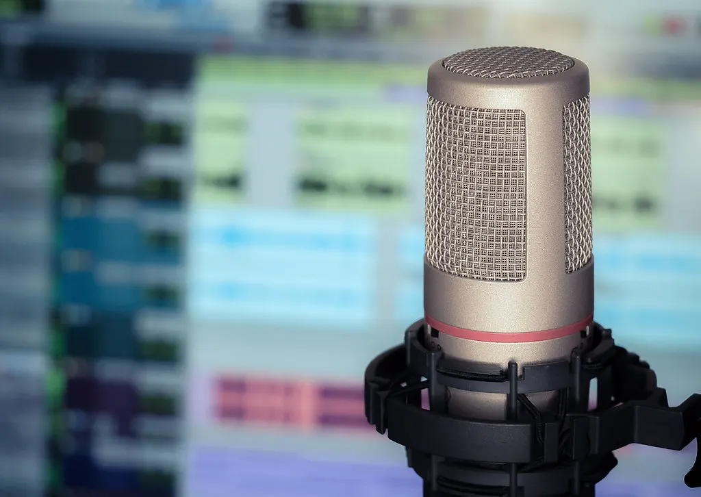 Microfoon op een statief in een podcaststudio, met op de achtergrond twee stoelen aan een tafel