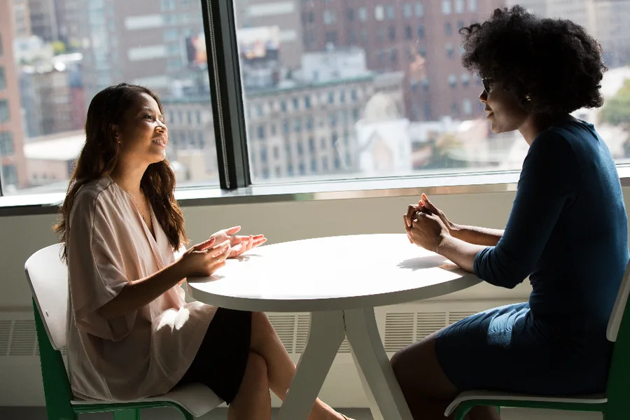 Twee vrouwen in gesprek aan een tafel bij een groot raam