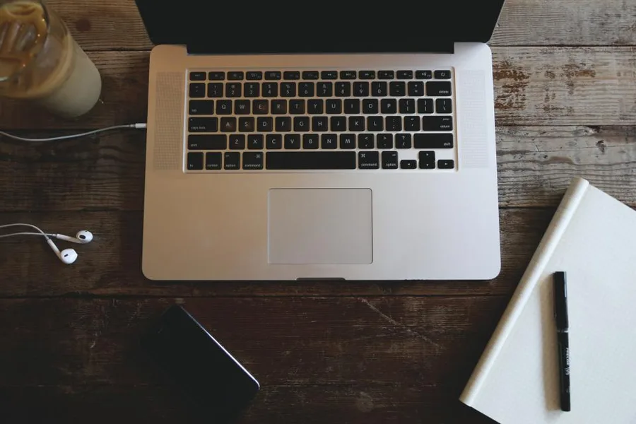Laptop met oordopjes en een notitieblok op een houten bureau