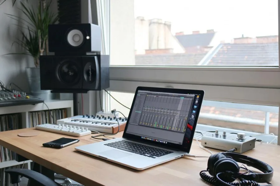 Thuisstudio met laptop, monitorboxen en een koptelefoon voor het raam